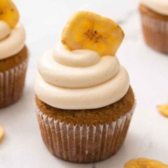 Three banana cupcakes with one in front and secret with banana chips scattered around.