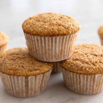 A couple bran muffins on a counter with one stacked on top of two muffins.