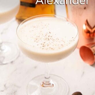 Pinterest graphic of a coupe glass of Brandy Alexander with cognac and shaker in the background some some nutmeg in front.