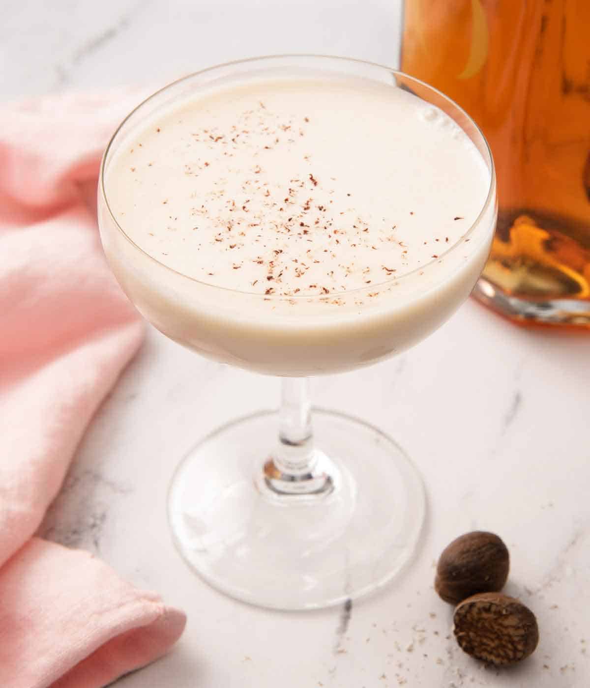 A glass of Brandy Alexander with fresh nutmeg shaved on top and some scattered beside it.