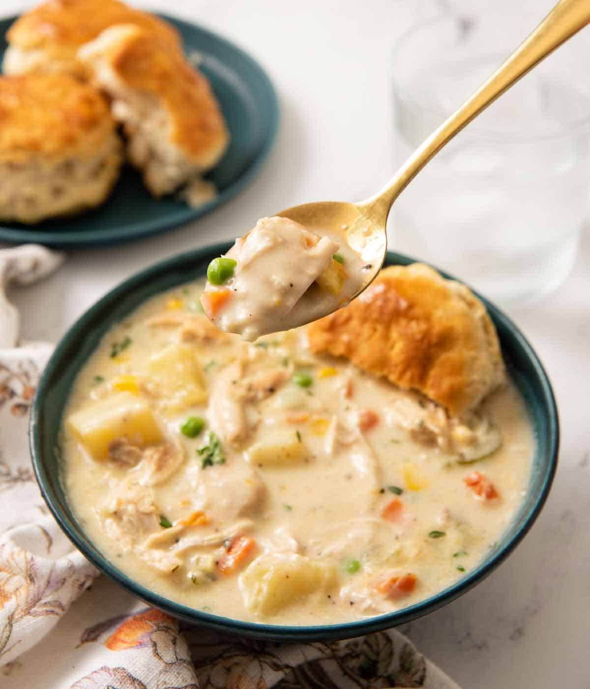 A spoonful of chicken pot pie soup lifted from the bowl with additional biscuits in the background.