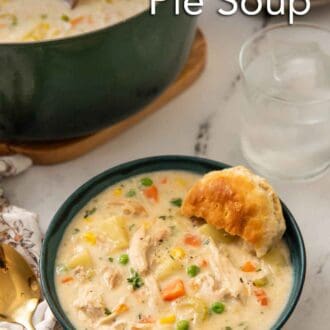 Pinterest graphic of a bowl of chicken pot pie soup with a glass of water, pot of soup, and plate of biscuits behind it.