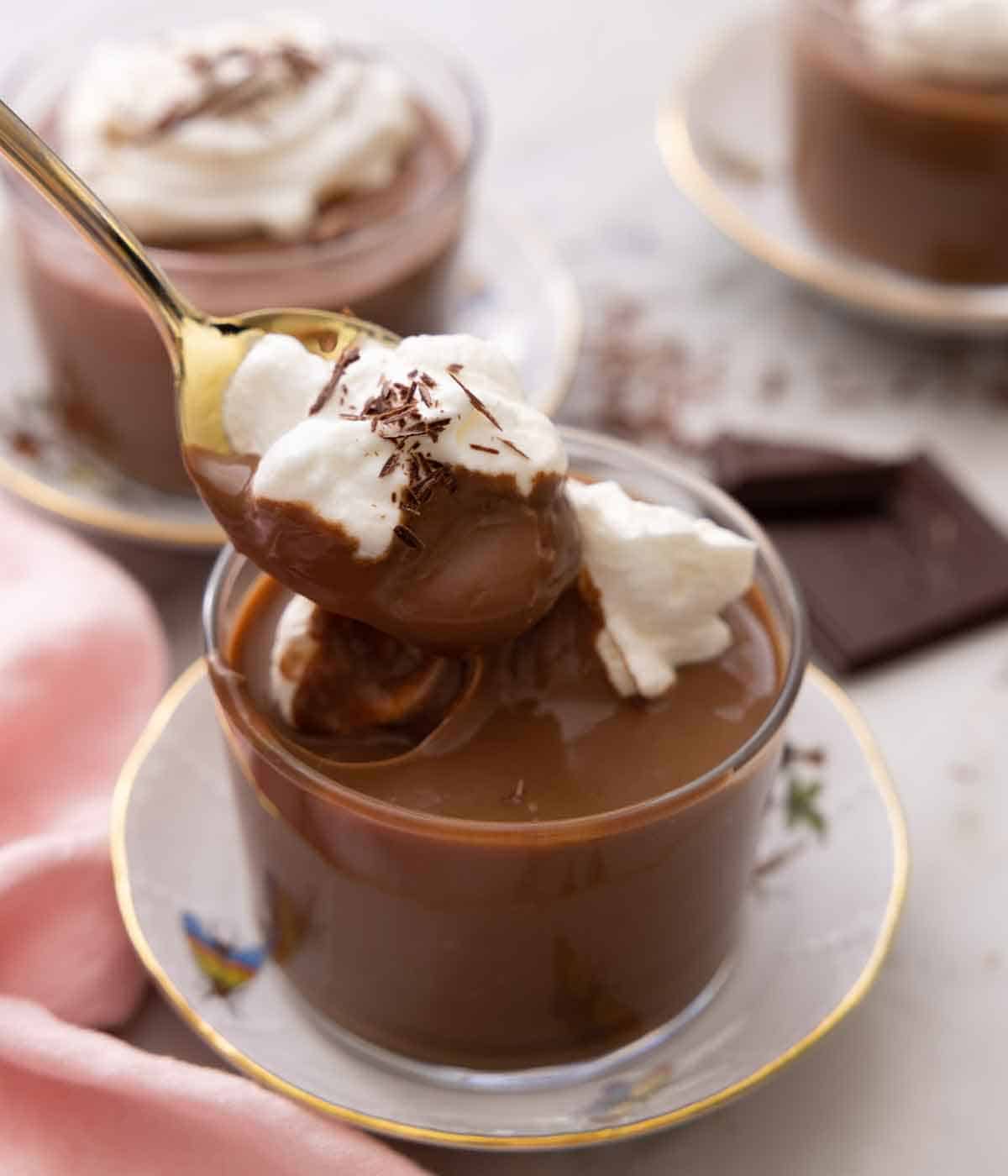 A spoonful of chocolate pudding with whipped cream being lifted out of the glass.