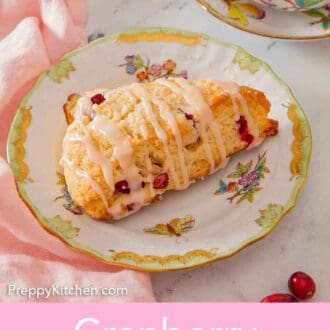 Pinterest graphic of a cranberry orange scone on a plate with a mug of coffee in the background.