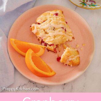 Pinterest graphic of a pink plate with a cranberry orange scone broken in half with two slices of oranges.