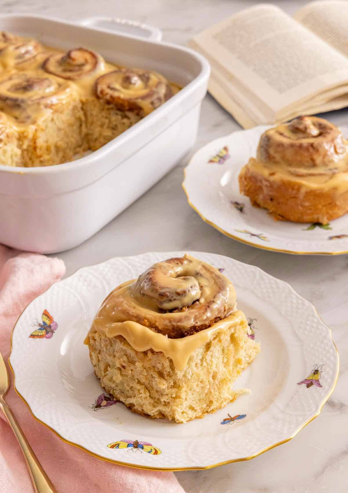 A plate with a piece of dulce de leche cinnamon roll with another in the background and the rest in a baking dish.