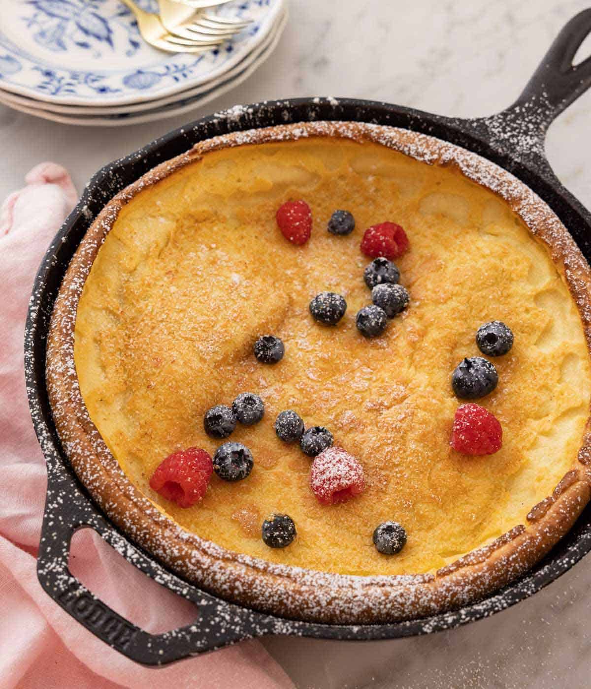 A cast iron skillet with Dutch baby, fresh berries, and powdered sugar on top.