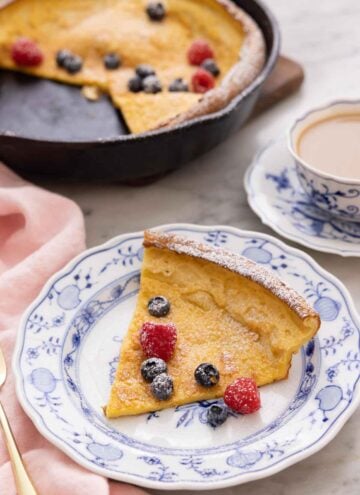 A plate with a slice of Dutch baby with fresh fruit and powdered sugar on top.