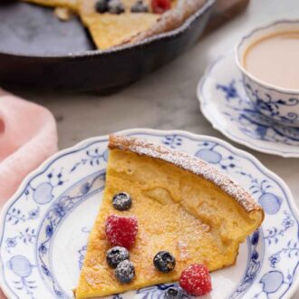 Pinterest graphic of a slice of Dutch baby with fresh berries and powdered sugar dusted on top.