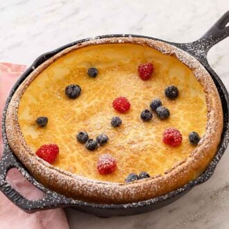 A cast iron skillet containing a Dutch baby with a bit of powdered sugar and fresh berries on top.