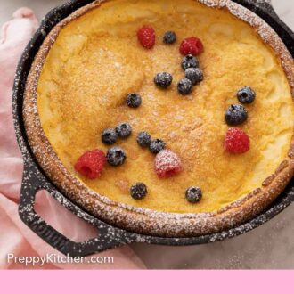 Pinterest graphic of a skillet with a Dutch baby and fresh blueberries and raspberries on top with a dusting of powdered sugar.