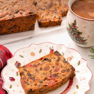 Pinterest graphic of a slice of fruit cake on a festive plate with a mug of coffee and more cake behind it.