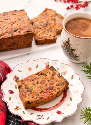 A festive plate with a slice of fruit cake with a mug of coffee and more cake behind it.