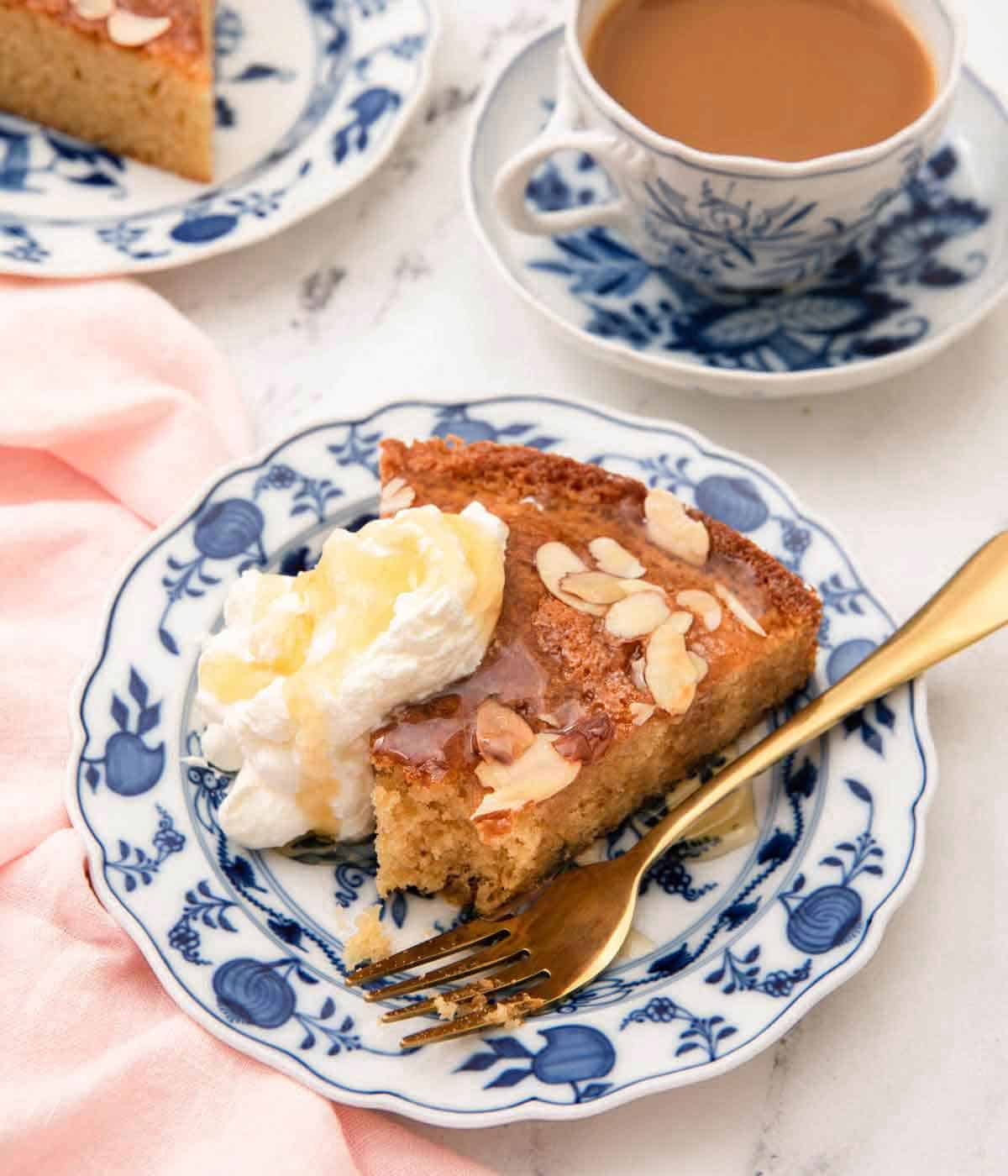 A plate with a slice of honey cake with whipped cream and a fork on the side with honey drizzled on top.