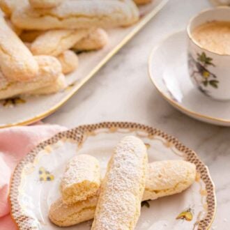 Pinterest graphic of a plate with a couple of ladyfingers with a cup of coffee and additional ladyfingers in the background.