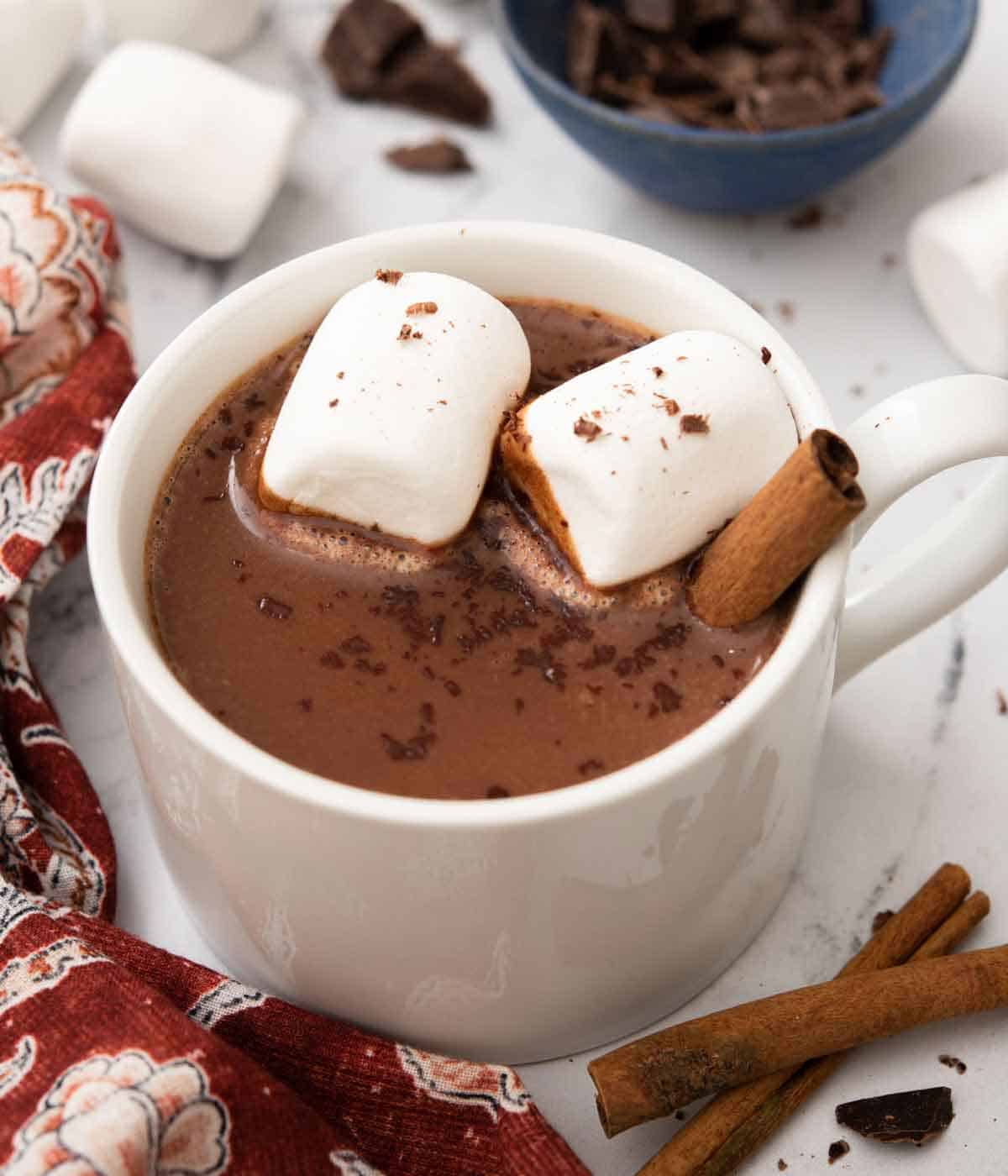 A white mug of Mexican hot chocolate with marshmallows and cinnamon stick inside.