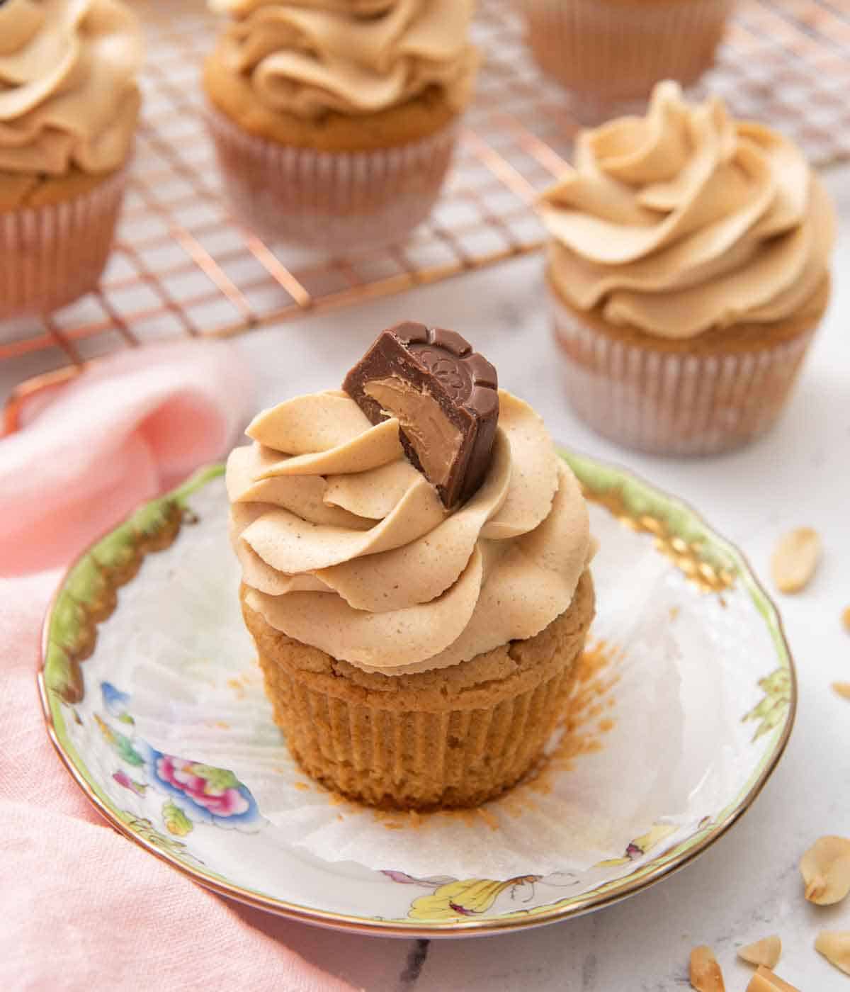 A plate with a peanut butter cupcake with the paper liner peeled opened with more cupcakes in the back.