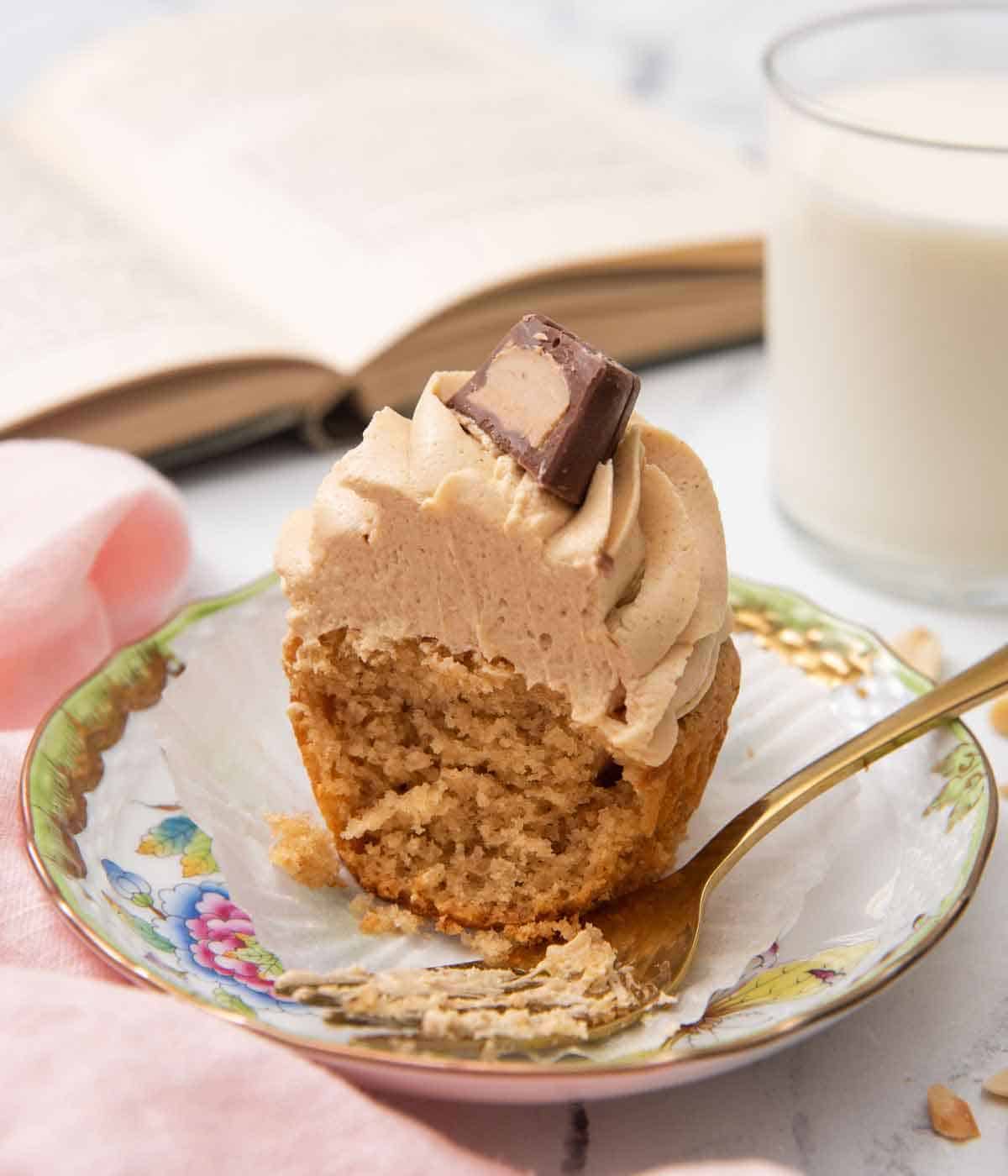 A small plate with a peanut butter cupcake where half is eaten with a fork beside the cupcake.