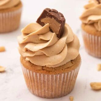 Three peanut butter cupcakes with one in the middle and in focus. Peanuts scattered around.