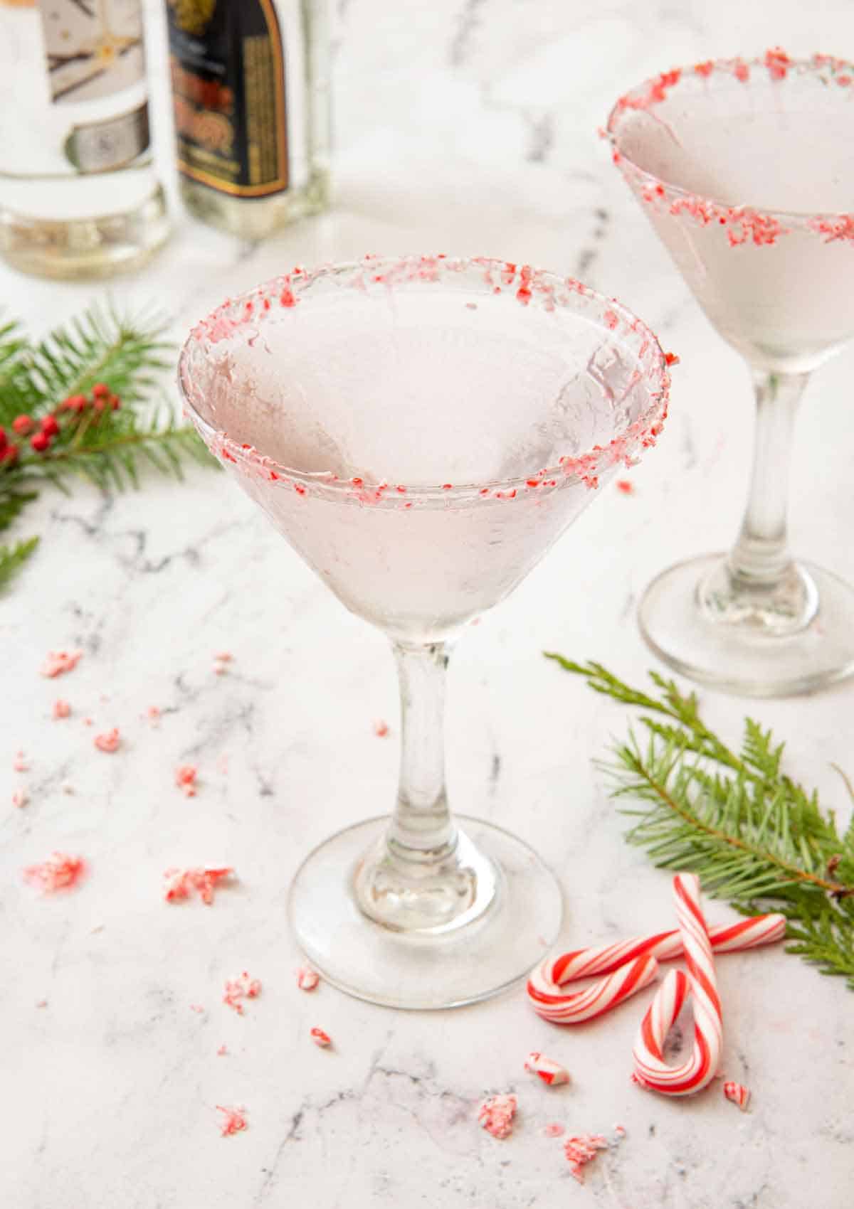 Two peppermint martinis with crushed and whole candy canes scattered around with festive garnishes on the counter.