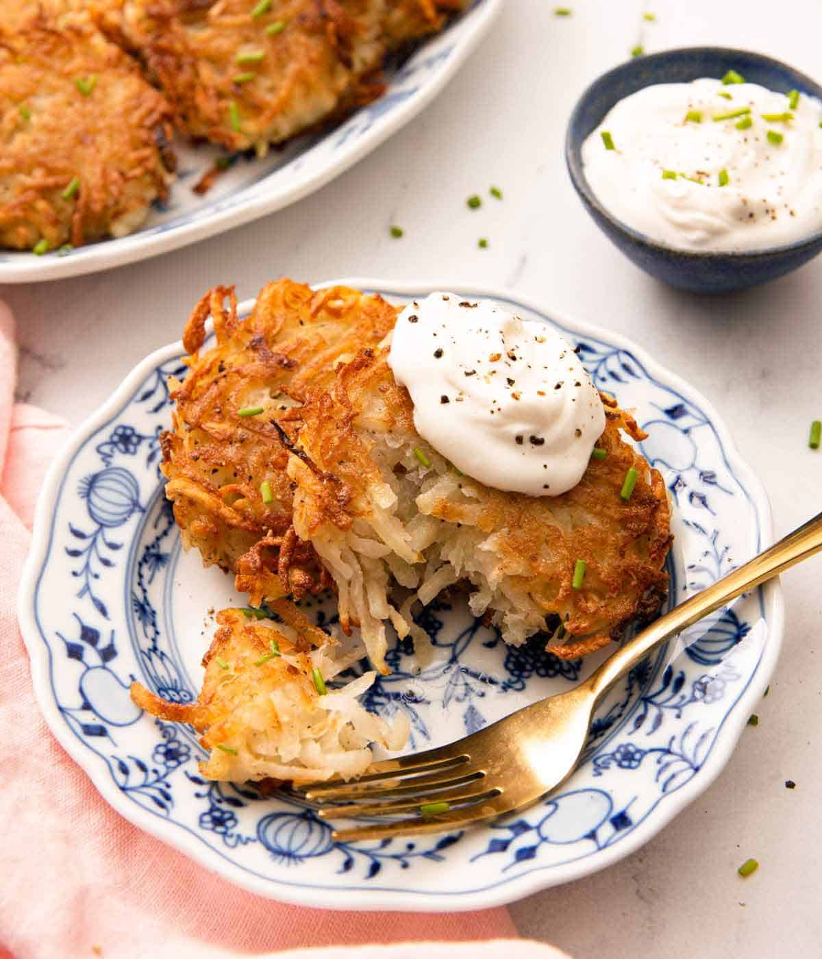 A plate with potato pancakes with sour cream on top with a piece torn off by a fork.