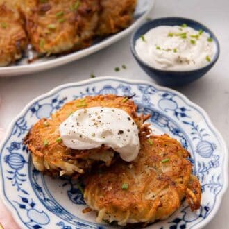 Pinterest graphic of a plate with two potato pancakes with sour cream on top and additional potato pancakes and dip in the background.