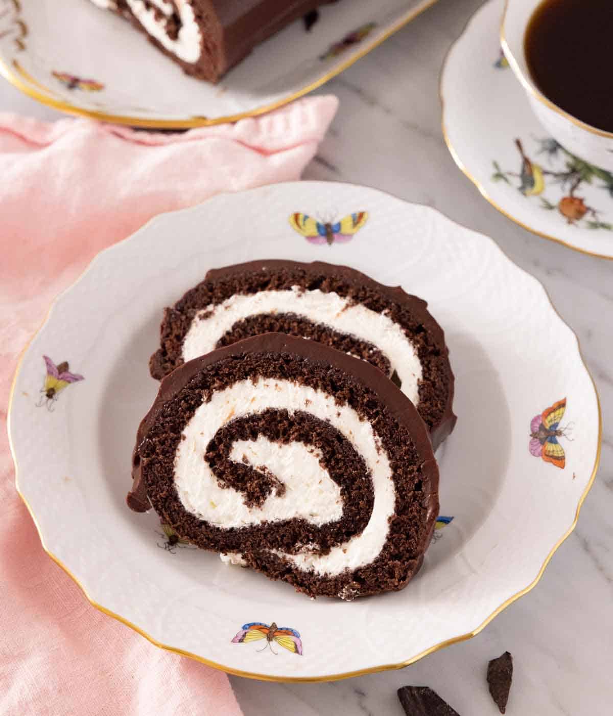 A plate with two slices of Swiss roll with a mug of coffee in the background.