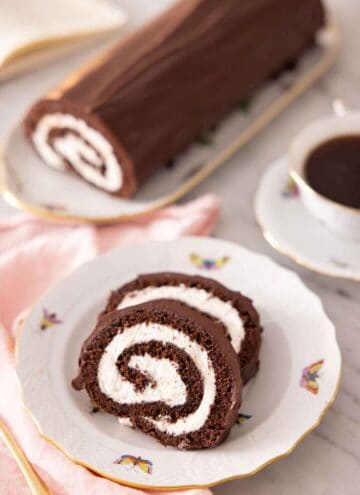 A plate with two slices of Swiss roll with the rest of the log in the background.