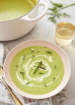 A bowl of asparagus soup with a drizzle of cream and garnished with dill and asparagus.