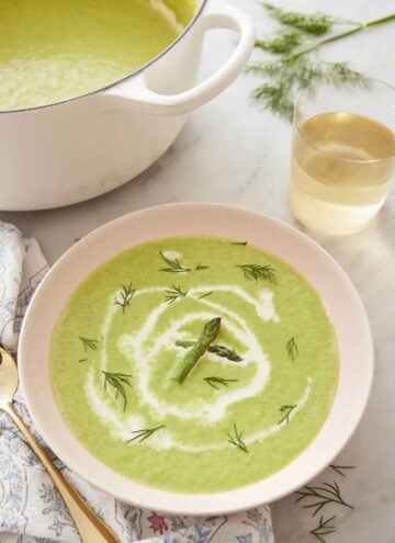 A bowl of asparagus soup with a drizzle of cream and garnished with dill and asparagus.