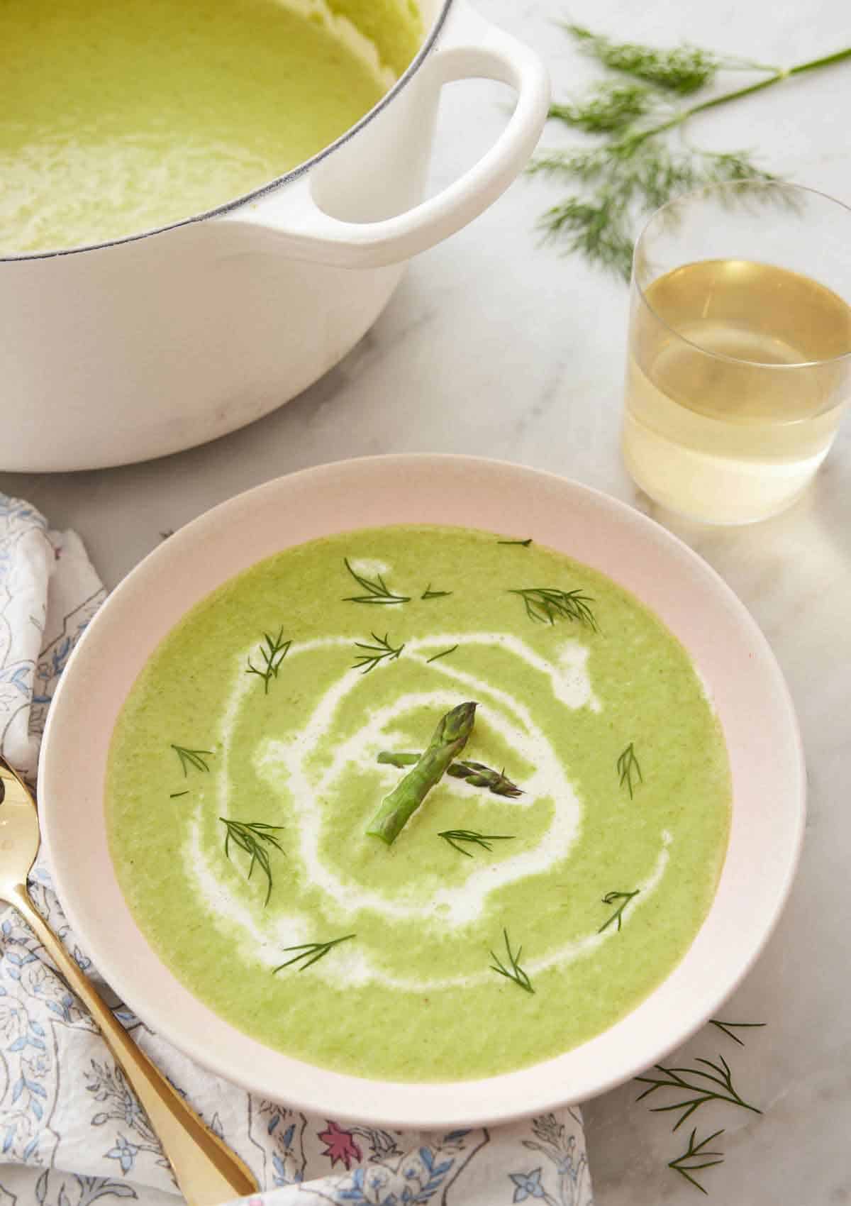 A bowl of asparagus soup with a drizzle of cream and garnished with dill and asparagus.