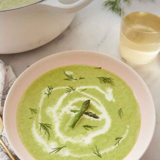 Pinterest graphic of a bowl of asparagus soup with a glass of wine and a large pot of soup in the background.