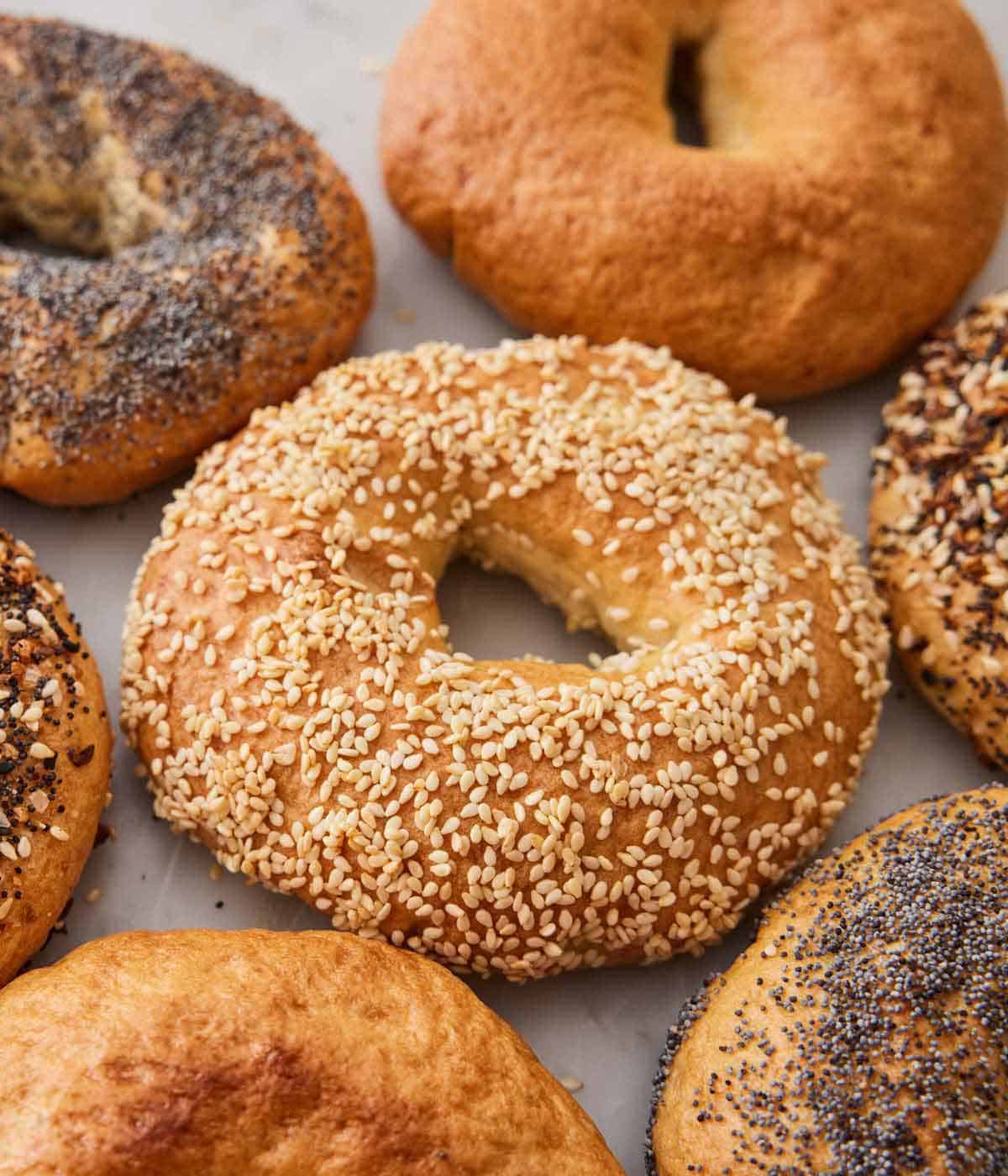 A bagel with sesame seeds surrounded by additional bagels with different toppings.