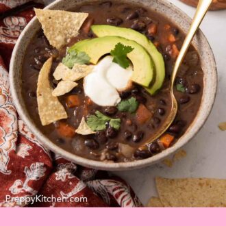 Pinterest graphic of a bowl of black bean soup with tortilla chips, sliced avocado, sour cream, and chopped cilantro.