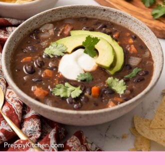 Pinterest graphic of a bowl of black bean soup with sliced avocado, sour cream, and cilantro as garnished.