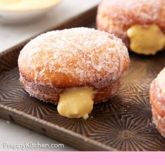Pinterest graphic of a baking sheet with bomboloni, with a close up on one with pastry cream oozing out.