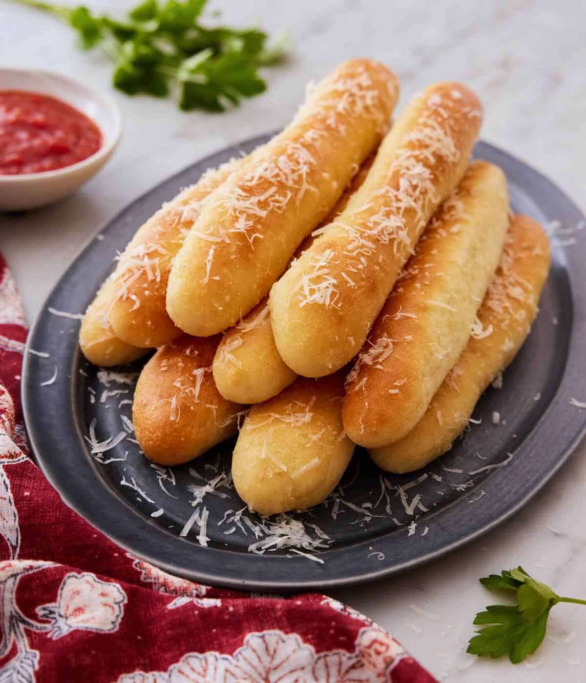 An oval platter with multiple breadsticks stacked on top of each other.