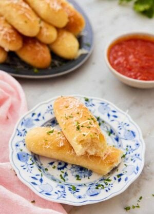 A plate with a breadstick torn in half with sauce and more bread in the background.
