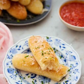 Pinterest graphic of a plate with a breadstick torn in half on a plate with sauce and more breadsticks in the back.