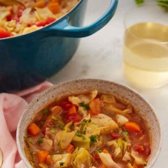 Pinterest graphic of a bowl of cabbage soup with a pot and drink in the back.