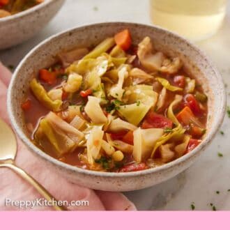 Pinterest graphic of a bowl of cabbage soup with a drink in the back and a second bowl of soup out of focus.
