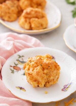 A plate with a cheddar biscuit on it with more in a platter in the background.