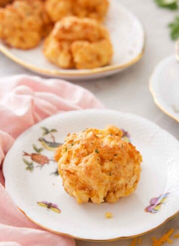 A plate with a cheddar biscuit on it with more in a platter in the background.