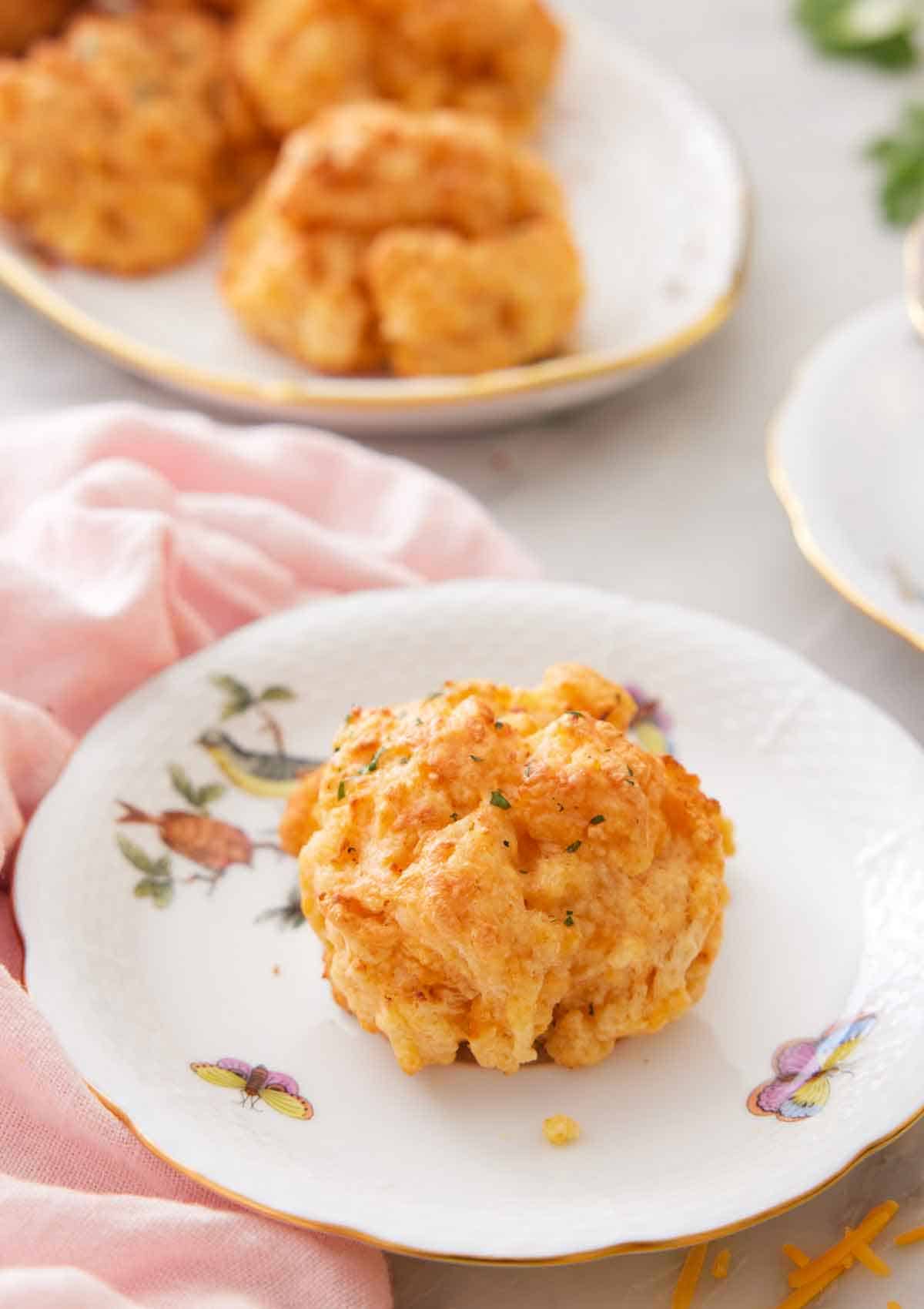 A plate with a cheddar biscuit on it with more in a platter in the background.
