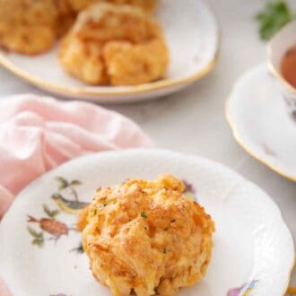 Pinterest graphic of a plate with a cheddar biscuit with more on a platter in the back.