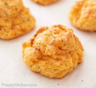 Pinterest graphic of a cheddar biscuit in focus with a couple more in the background.