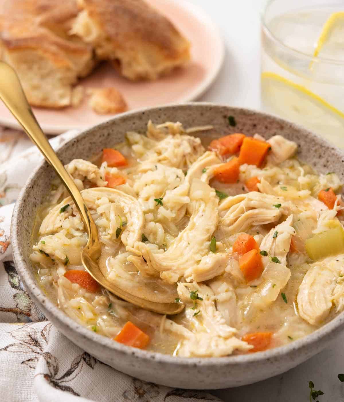 A bowl of chicken and rice soup with a spoon tucked in.