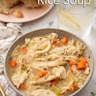 Pinterest graphic of a bowl of chicken and rice soup with lemon water and bread in the background.