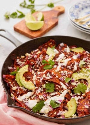 A cast iron skillet with chilaquiles topped with sliced avocado and cilantro.