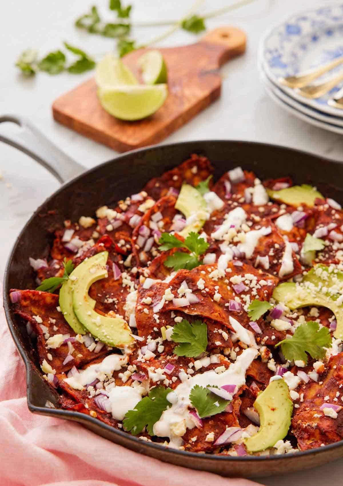 A cast iron skillet with chilaquiles topped with sliced avocado and cilantro.